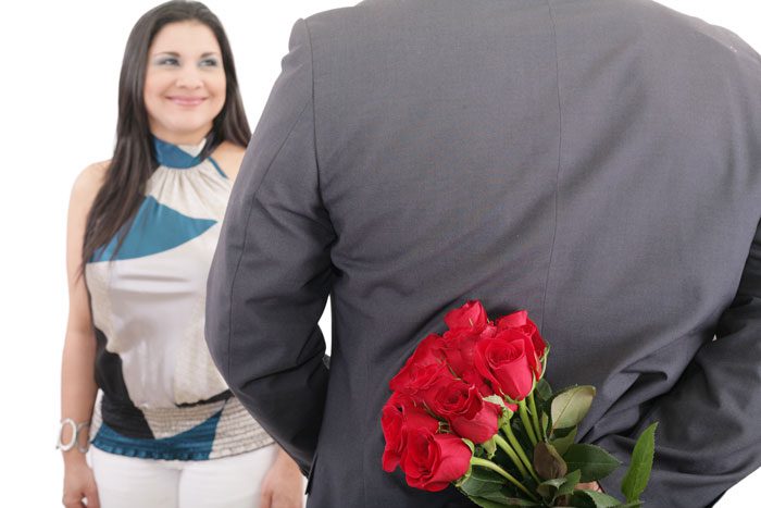 man hiding red rose bouquet behind his back