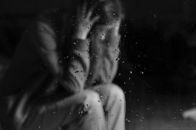 upset woman seen through glass with rain on it - black and white
