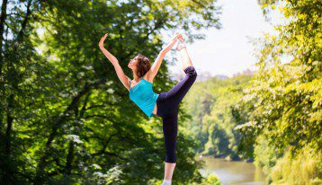 woman doing advanced yoga in a park near a river
