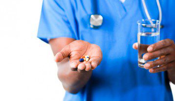 nurse in blue scrubs holding out pills and glass of water