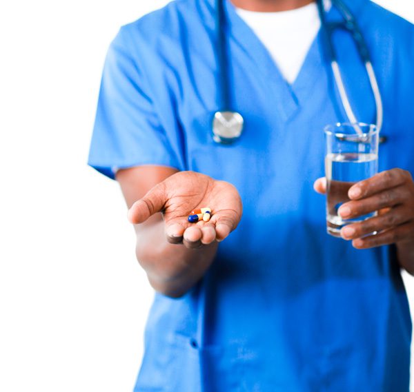 nurse in blue scrubs holding out pills and glass of water