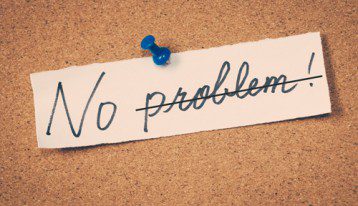 scrap of paper pinned to corkboard that says 'No Problem' with 'problem' crossed out