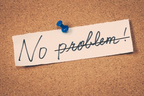 scrap of paper pinned to corkboard that says 'No Problem' with 'problem' crossed out