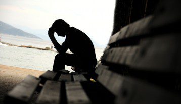 depressed man on bench near ocean