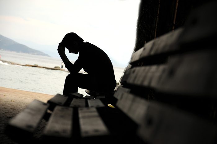 depressed man on bench near ocean