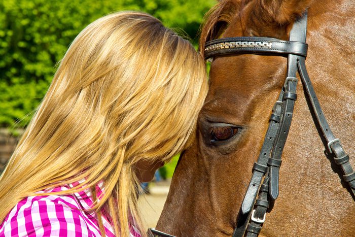 blonde woman with head pressed against horse's forehead