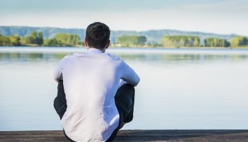 man sitting at the edge of a lake with back to camera