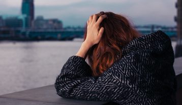 upset red headed woman looking over concrete railing near water