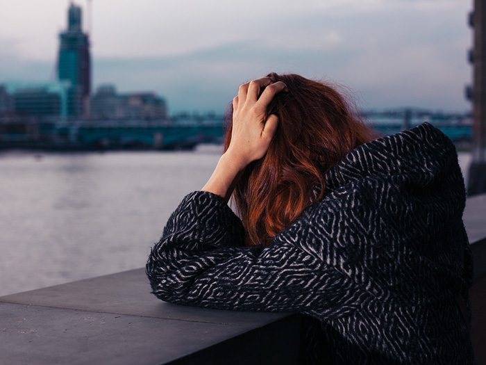 upset red headed woman looking over concrete railing near water