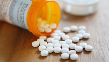 small round white pills spilling out of prescription bottle