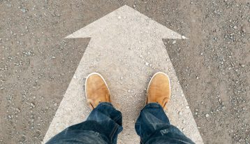 feet standing on arrow painted on dirt road