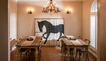 lovely dining room with two long wooden tables with chairs and chandelier; curtains have horse silhouette