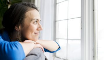 smiling woman looking out house window - transitional