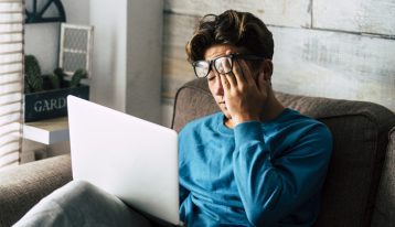 tired teenage boy on laptop rubbing his eyes - your college student