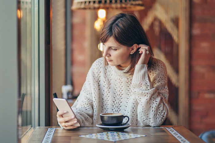 woman in cafe looking at cell phone - alcohol treatment