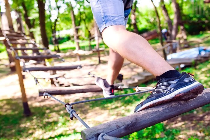 close up of man doing a low ropes course in the woods - experiential therapy