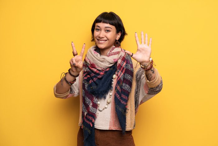 smiling young woman holding up hand sign for number seven on yellow background - residential treatment