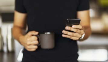 man holding a cup of coffee and dialing cell phone - pay for addiction treatment