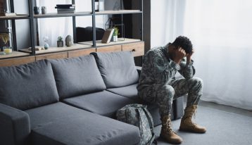 young Black man in military fatigues sitting on couch at home - veterans and addiction