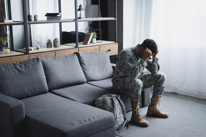 young Black man in military fatigues sitting on couch at home - veterans and addiction