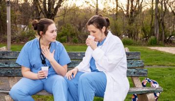 two female healthcare workers talking on a bench outside - healthcare workers