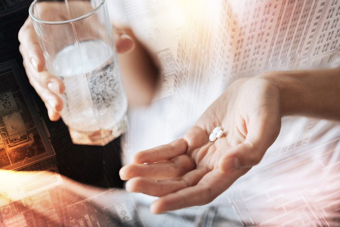 woman's hand with 3 small white pills and a glass of water in the other hand - oxymorphone