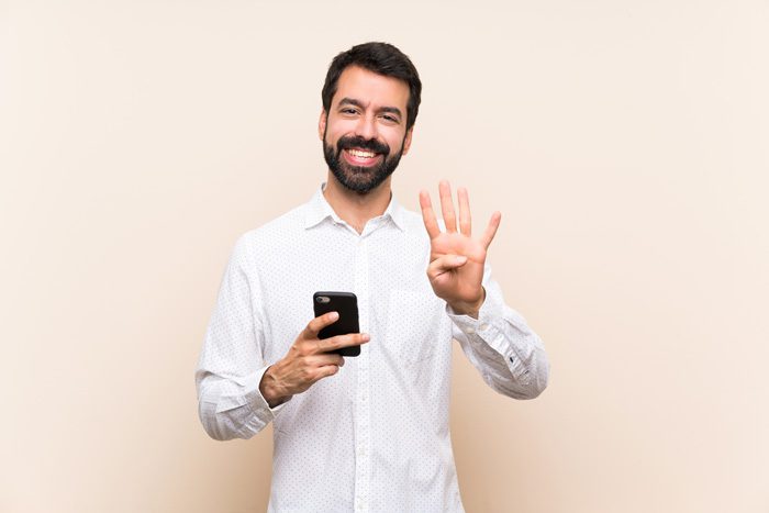 handsome, smiling man holding his cell phone and using his other hand to signal the number four - inpatient treatment