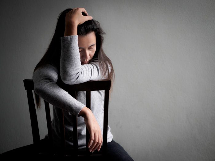 sad woman sitting backward in a wooden chair - depression and drug use