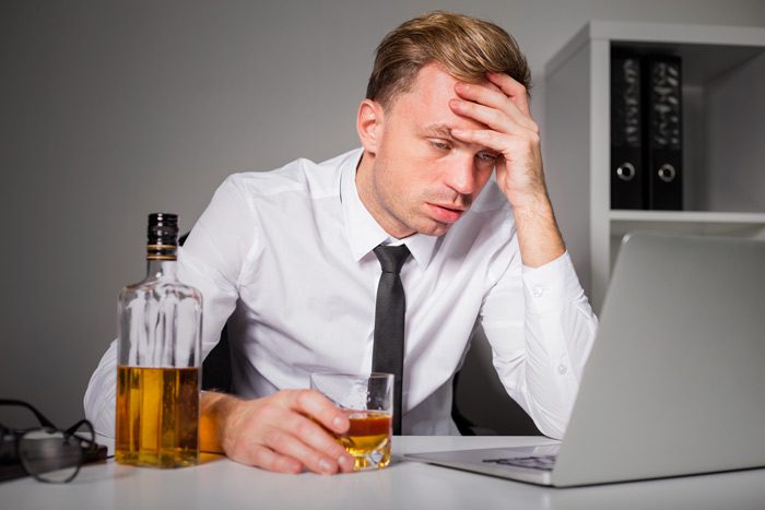 business man sitting at his desk drinking liquor - alcohol at work