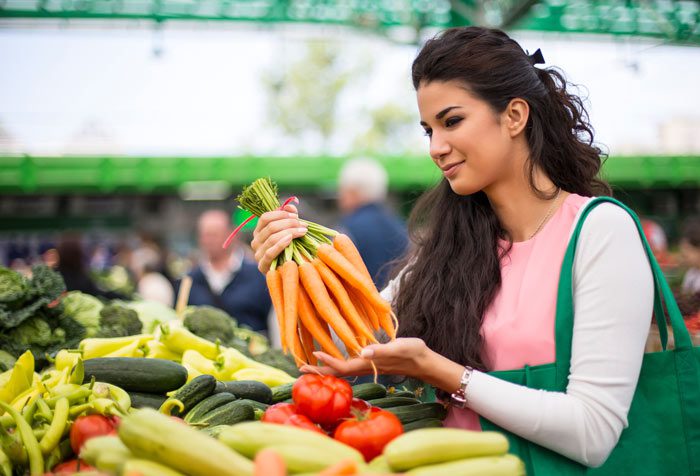beautiful Latina woman holding a bunch of carrots in the produce section of a grocery store - exercise