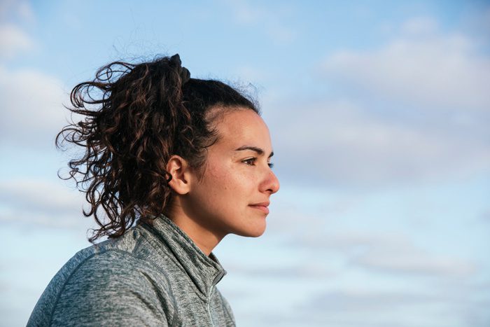 pretty brunette young woman looking forward with the sky behind her - alumni support