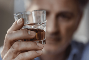 A man looking at a glass of alcohol.