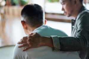 Man placing a supportive hand on another man’s shoulder, offering comfort and understanding during an emotional moment.