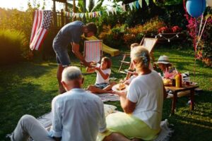 Multi-generation family on picnic in back yard sitting on blanket, eating burgers and celebrating