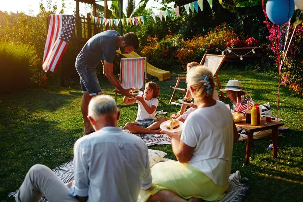 Multi-generation family on picnic in back yard sitting on blanket, eating burgers and celebrating