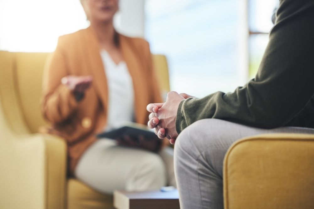 Close-up of a therapy or counseling session, showing two people seated across from each other, with one person speaking and the other listening attentively.