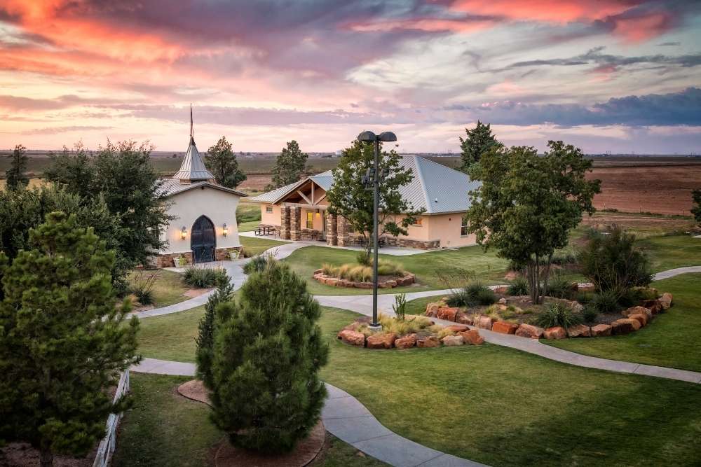 Ranch at Dove Tree, facility with landscaped gardens, walking paths, and buildings surrounded by trees under a colorful sunset sky.