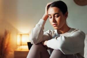 Woman sitting indoors with eyes closed, resting her head on her hand, looking thoughtful or stressed.