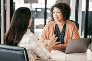 Two women talking at a desk.