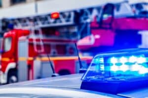 Close-up of a police car’s blue emergency lights with a fire truck in the background.