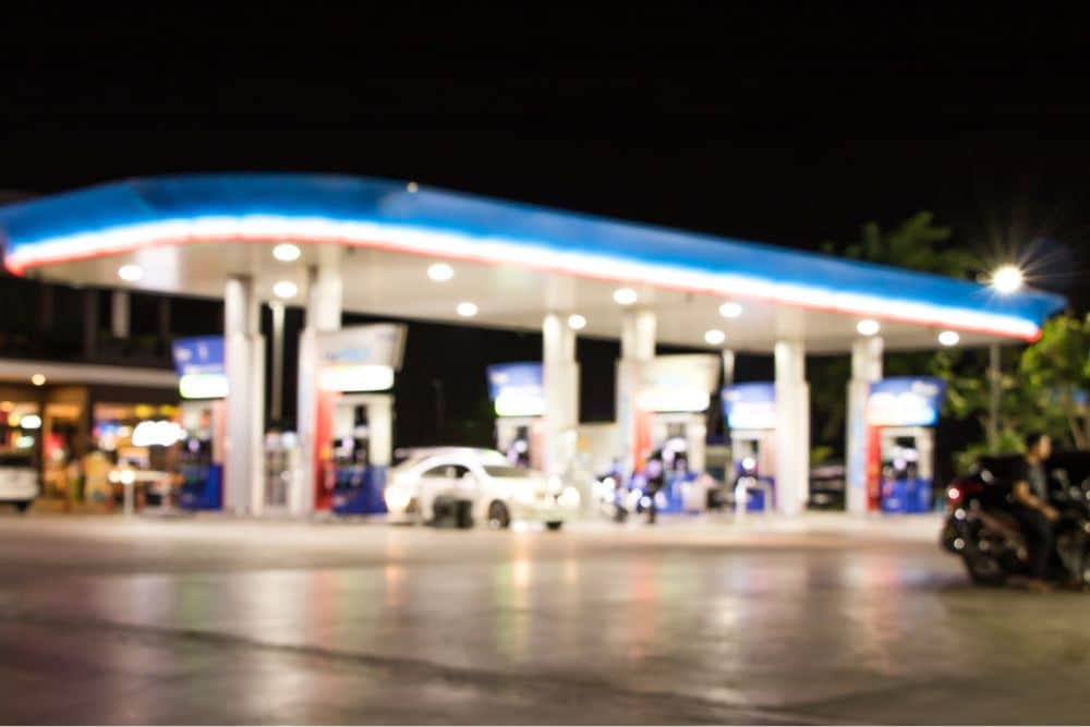 A brightly lit gas station at night with cars parked near the pumps, symbolizing the sale of dangerous substances like “gas station heroin.”